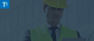 Um homem vestindo equipamento de proteção, como um capacete e um colete, ele está concentrado, olhando para o tablet